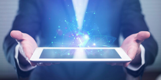 Person in a suit holding a tablet, above which a glowing, connected digital pattern in blue and purple is hovering.
