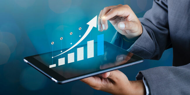 Person in a suit holding a tablet with an overlaid bar chart and upward-pointing arrow, currency symbols along the curve.